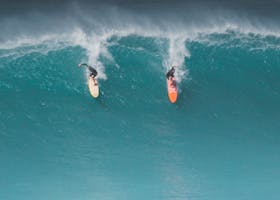 Two surfers ride massive waves in Hawaii, capturing the thrill of ocean sports.